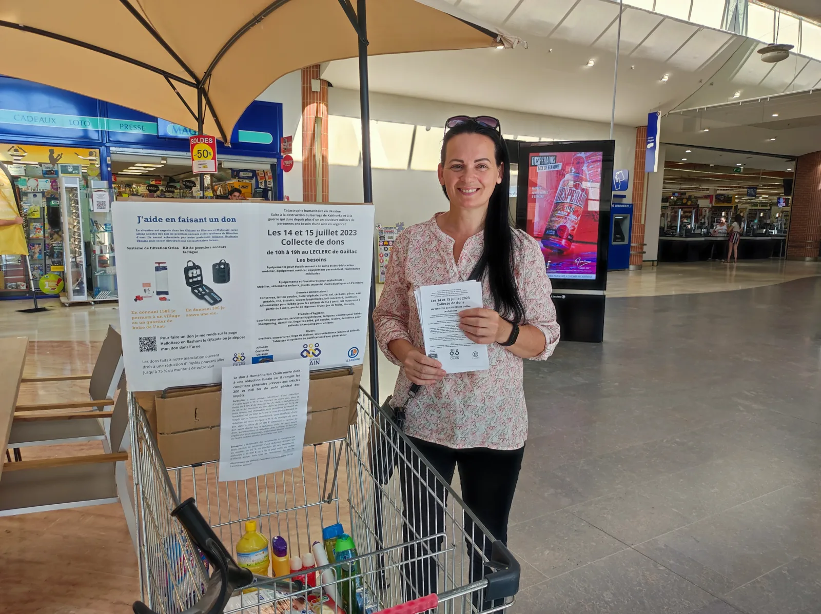 Une bénévole de l’association à un point de collecte de dons dans un centre commercial, à côté d’un chariot